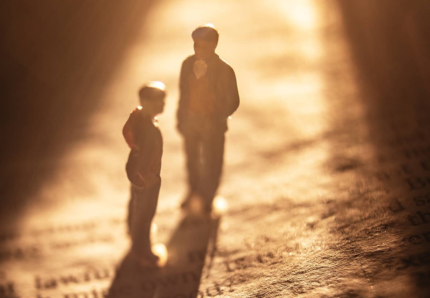 Small figurines of a parent and child standing on a page of scripture bathed in golden light.