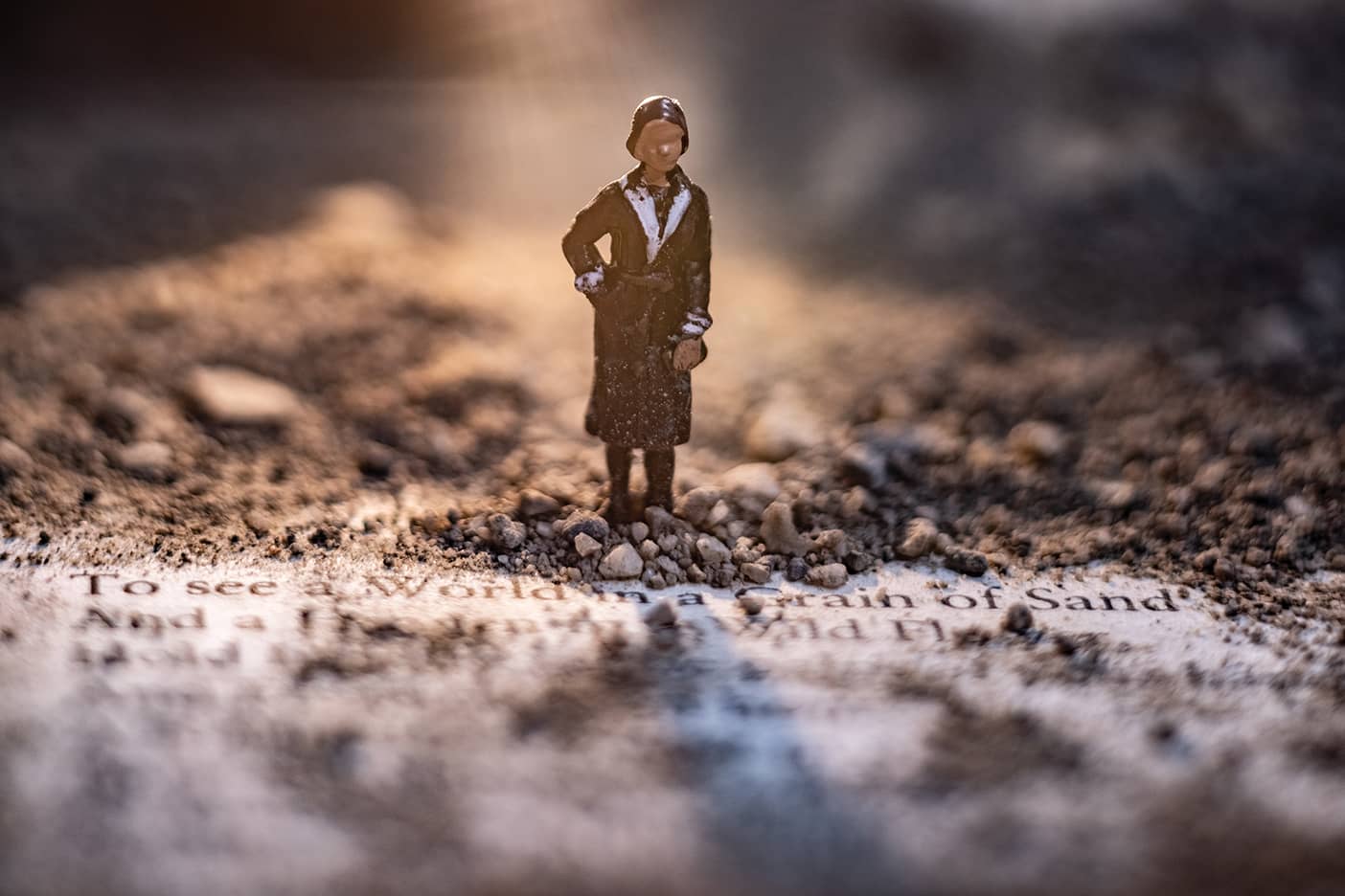 A small female figurine stands on a page of poetry, bathed in muted golden light.