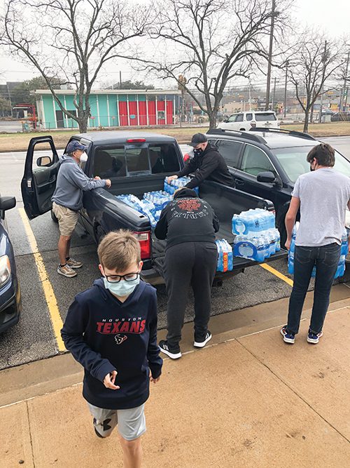Five volunteers unload cases of water bottles from the back of a pickup truck.