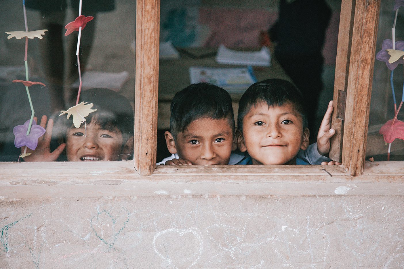 Three smiling Bolivian children look at the camera through a window.