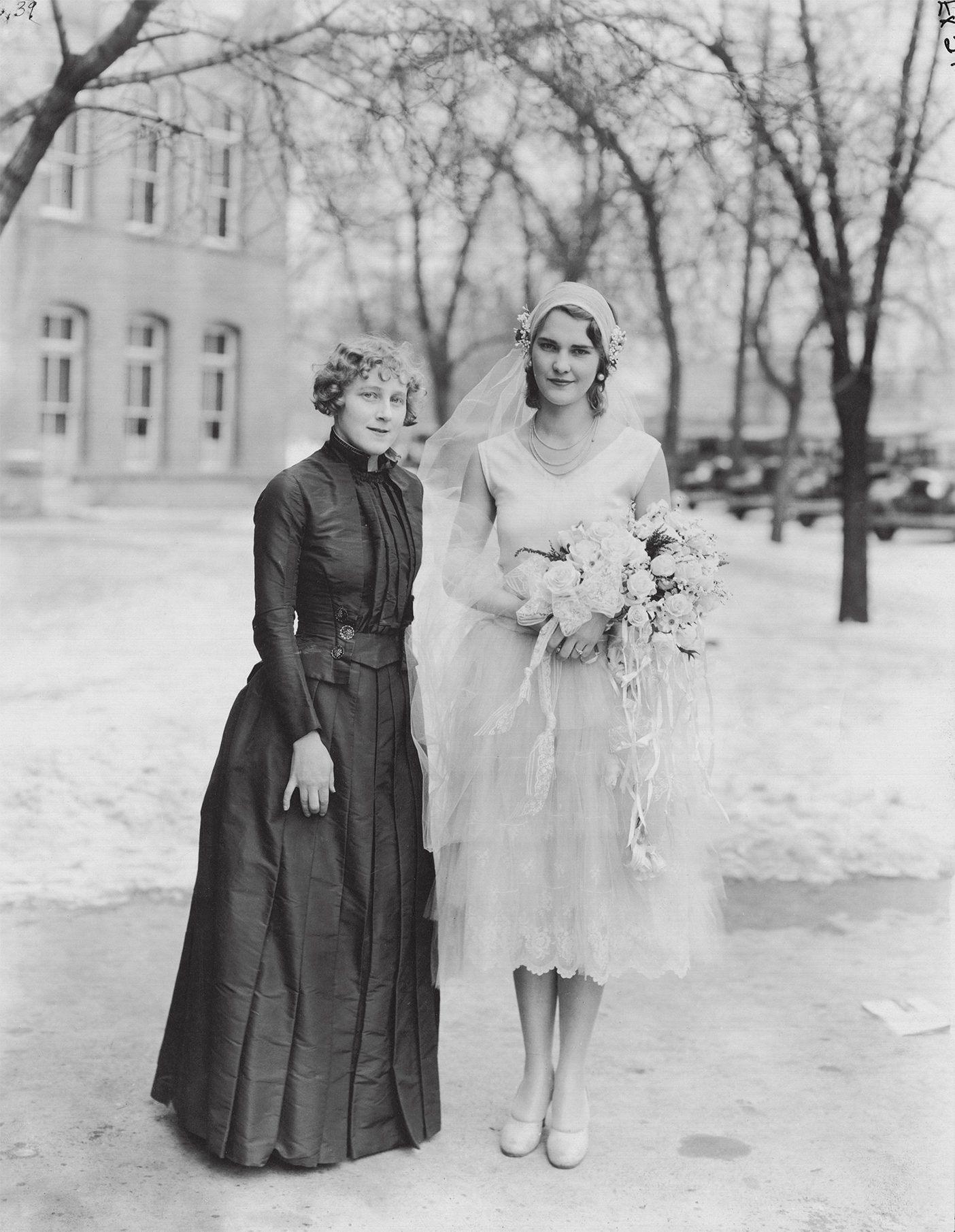 Two girls stand outside of the Training Building in the 1920s wearing handmade dresses.