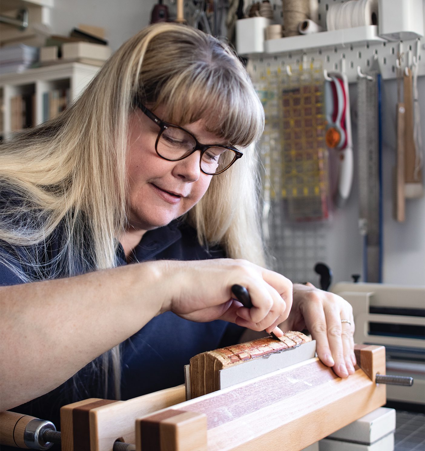 Blonde woman working with a tool on printing objects to repair books.