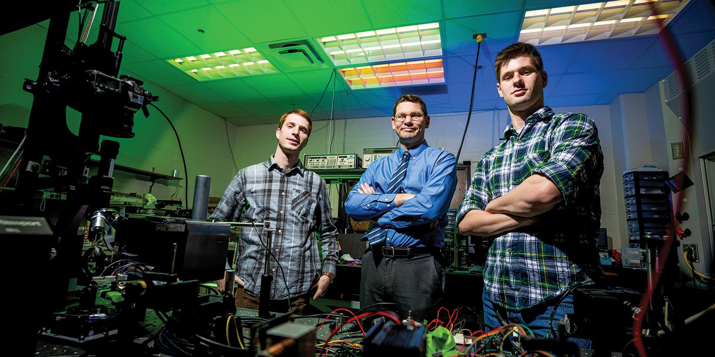 Professor Dan Smalley stands in his lab in between two of his student researchers, Erich J. Nygaard on the left and Wesley R. Rogers on the right.