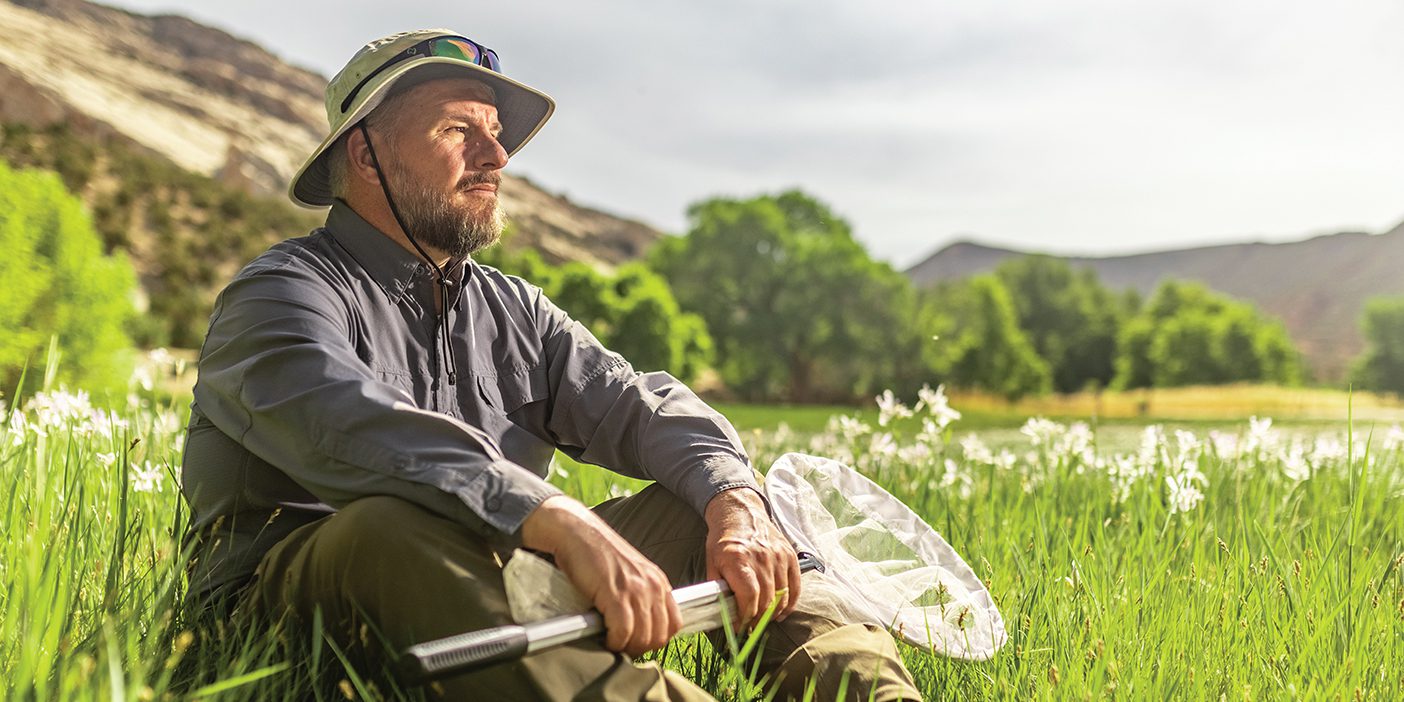 Jim Spencer sits in the grass holding a buttefly net.