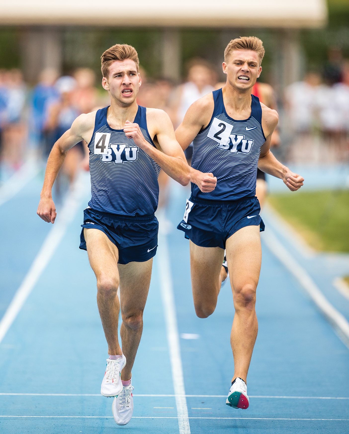 Two BYU runners, Casey Clinger and Lucas Bons, run next to each other on the track with exertion showing on their faces.