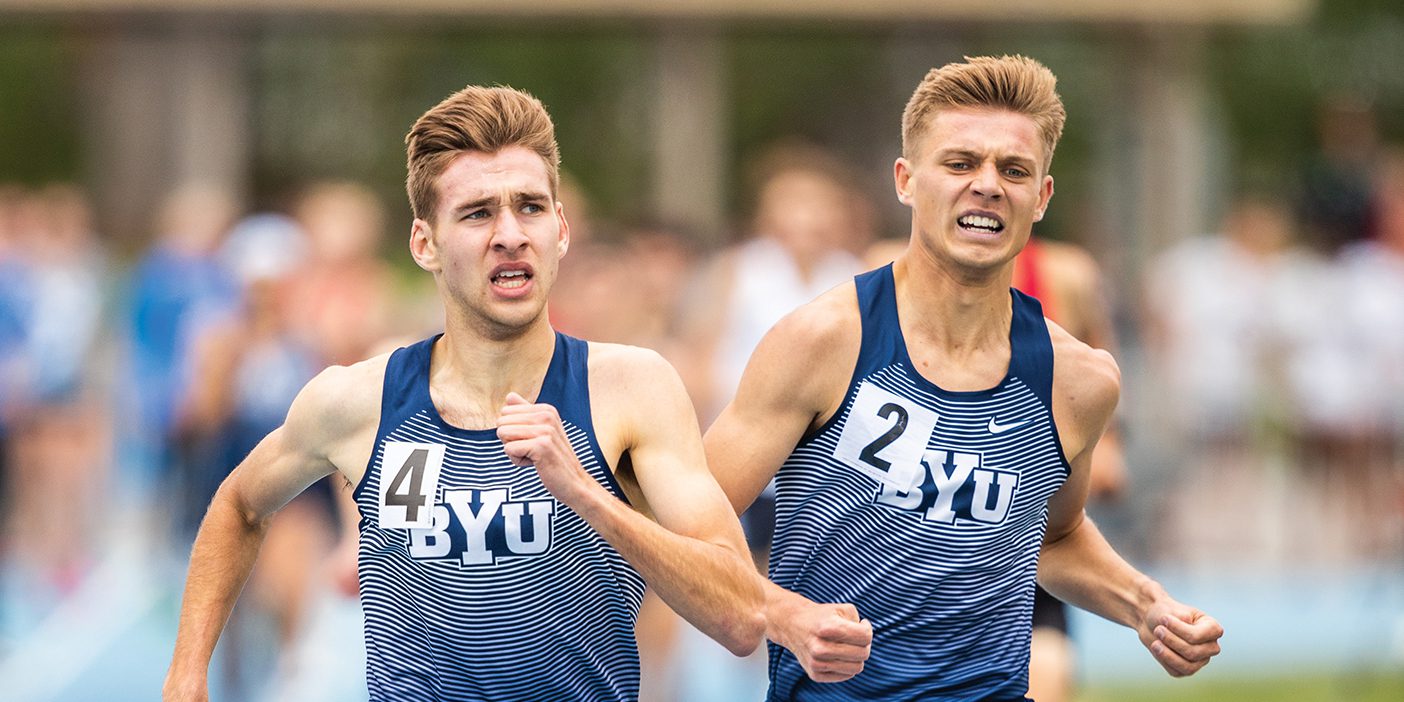 Two BYU runners, Casey Clinger and Lucas Bons, run next to each other on the track with exertion showing on their faces.