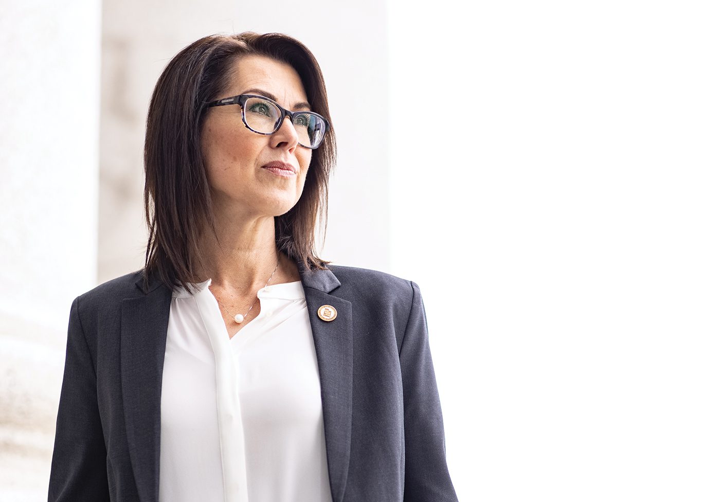 Deidre Henderson stands in a powerful pose with her hands in her pockets, wearing a white shirt and blue jacket and looking confidently off into the distance to her left.