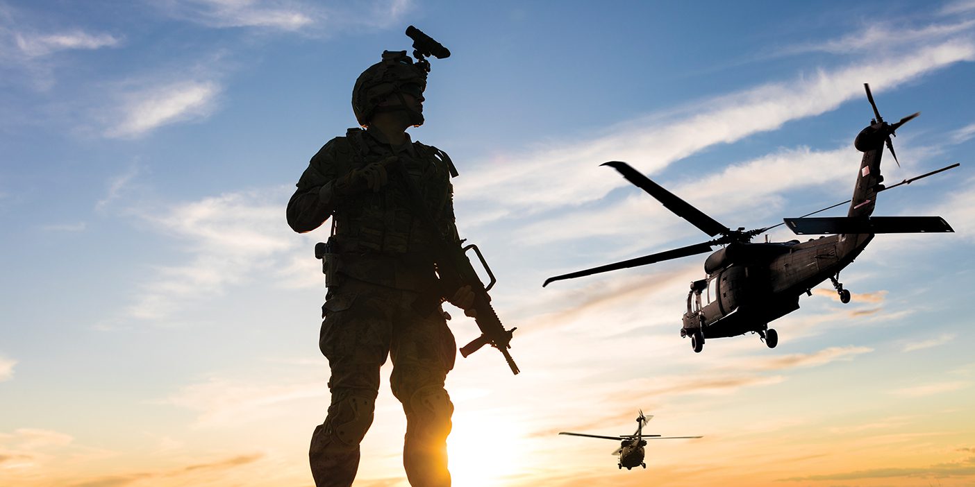 Soldier standing on the battlefield looking into the sky at helicopters.