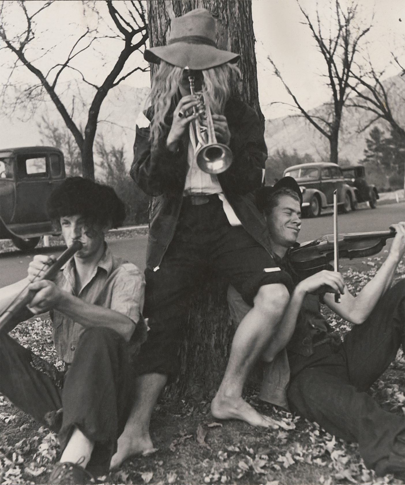 A black and white photo from the 1940s of three BYU students dressed up in hobo costumes and playing instruments.
