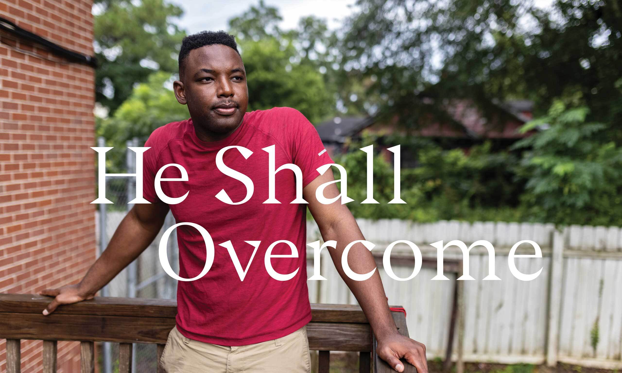 A Black man stands on a deck with a red brick building and green trees in the background. Overlaid text reads, "He Shall Overcome."