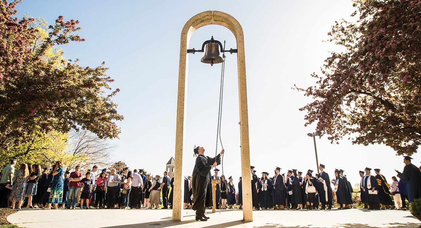 A graduate rings a bell outside the Marriott Center.