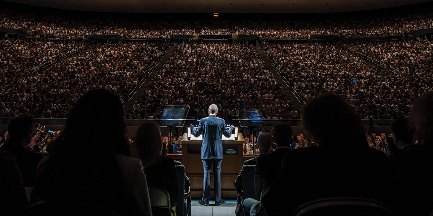 A photo taken from behind the podium of a speaker addressing a crowd at the Marriott Center.