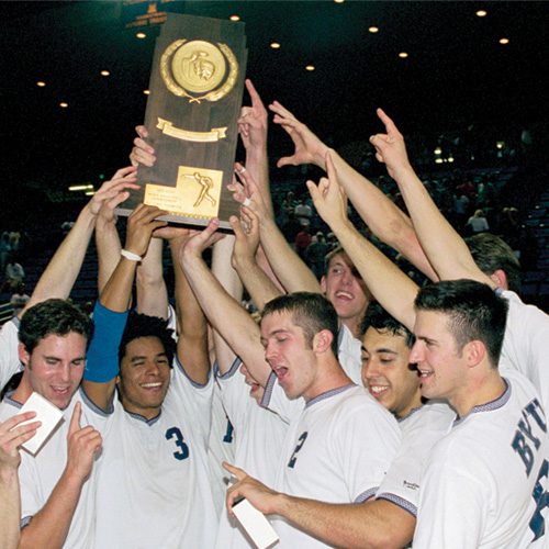 The men's volleyball team lifts up a trophy and cheer.