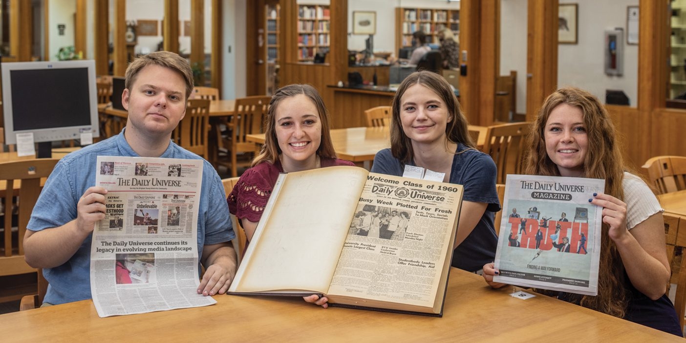 A group of students hold up various copies of newspapers and magazines.