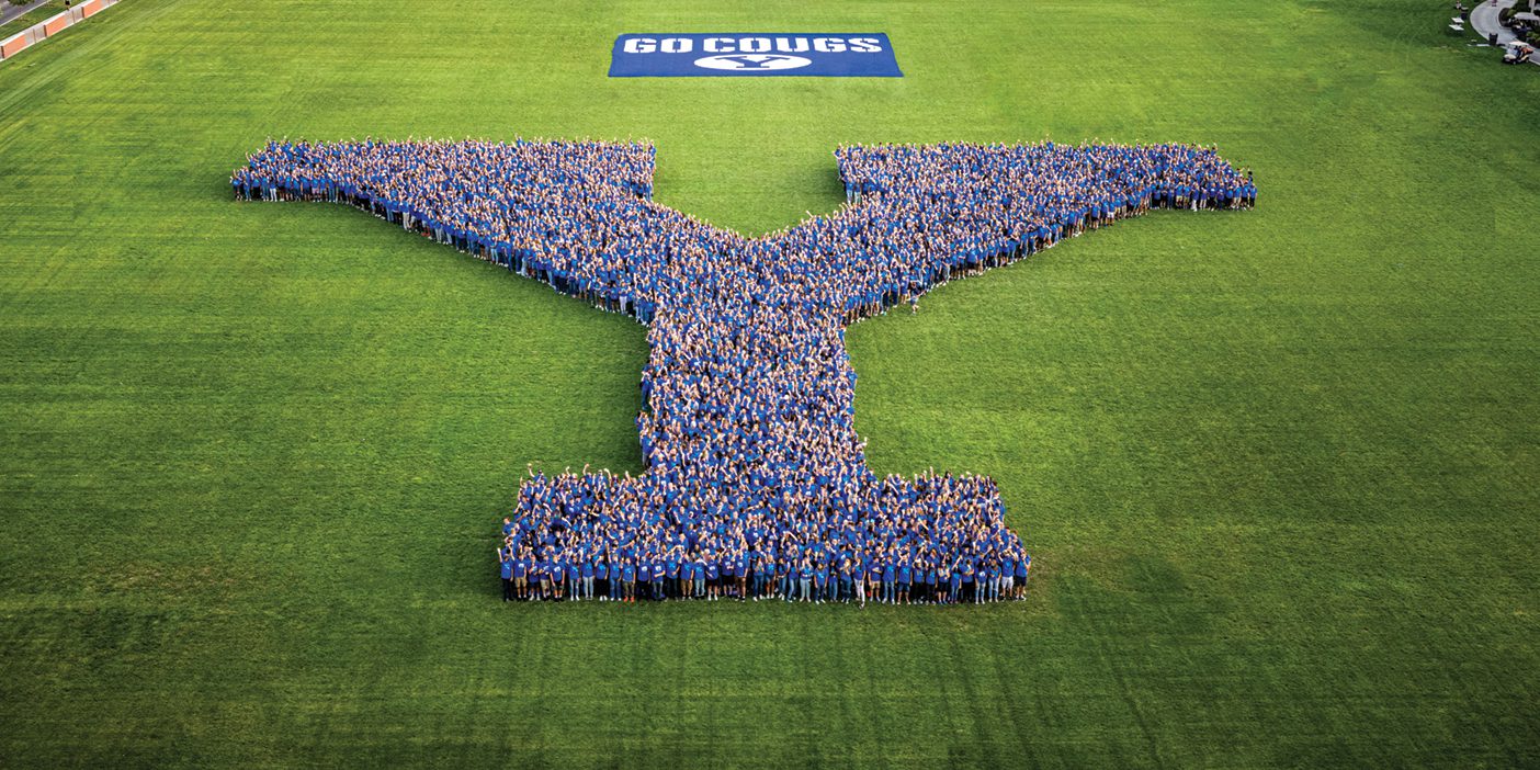 A photo of students wearing blue and standing in a Y formation on the football field.