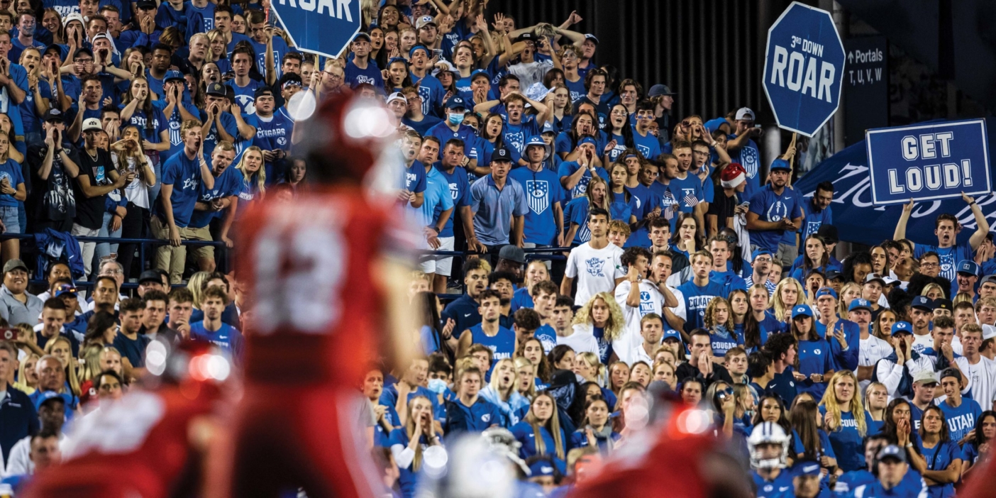 University of Utah football players dressed in red play in front of boisterous BYU fans mostly dressed in blue.