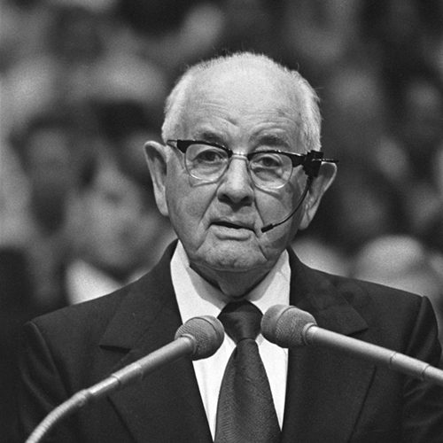 A black and white photo of President Spencer W. Kimball speaking into two microphones in 1975.