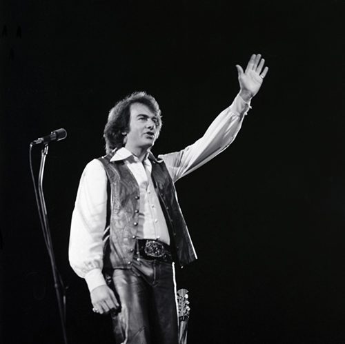 A black and white photo of Neil Diamond waving at a concert.