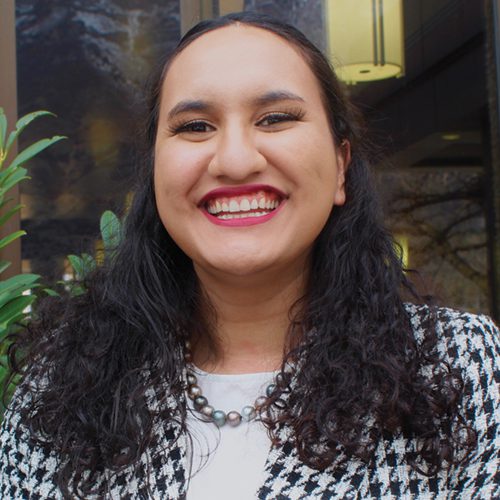 An woman with dark curly hair and a houndstooth blazer smiles.