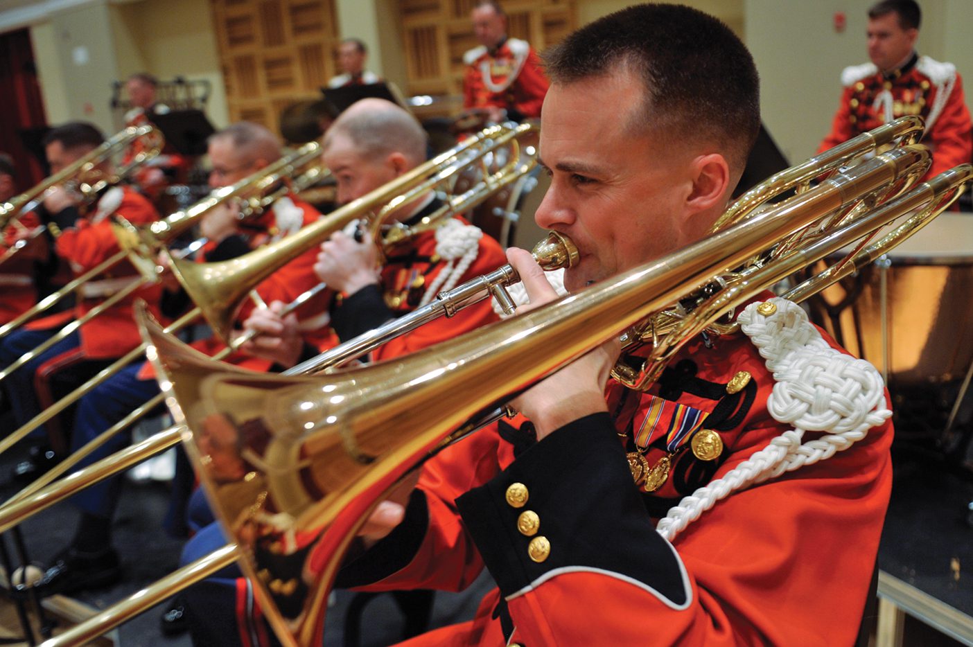 A man in a red, decorative military jacket plays the bass trombone.