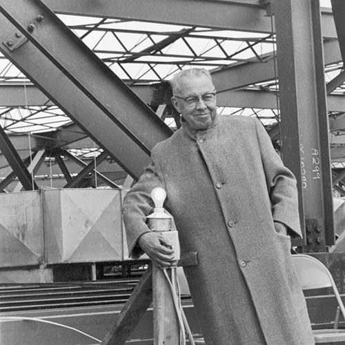 A man in a long coat flips a switch among scaffolding.