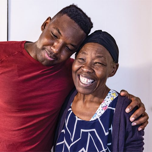 A Black man puts his arm around an older Black woman, who is smiling.