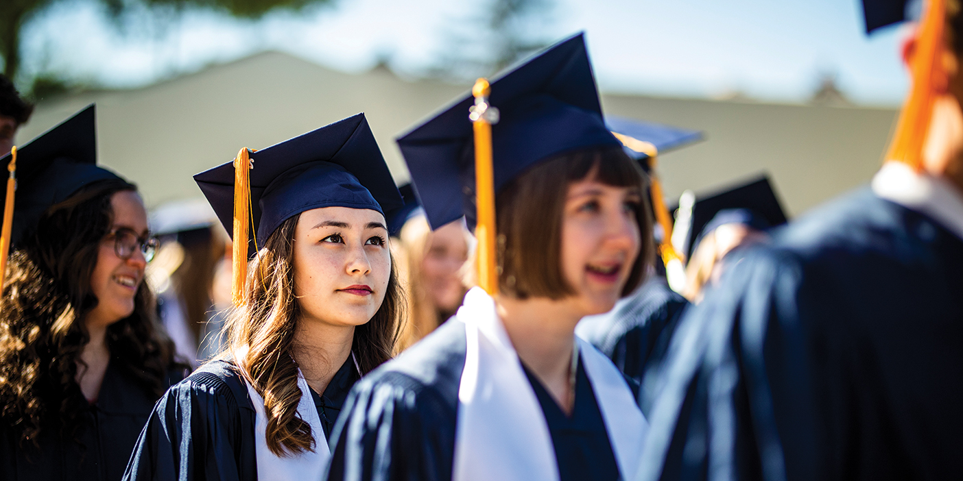 BYU graduates in cap and gown march toward the Marriott Center.