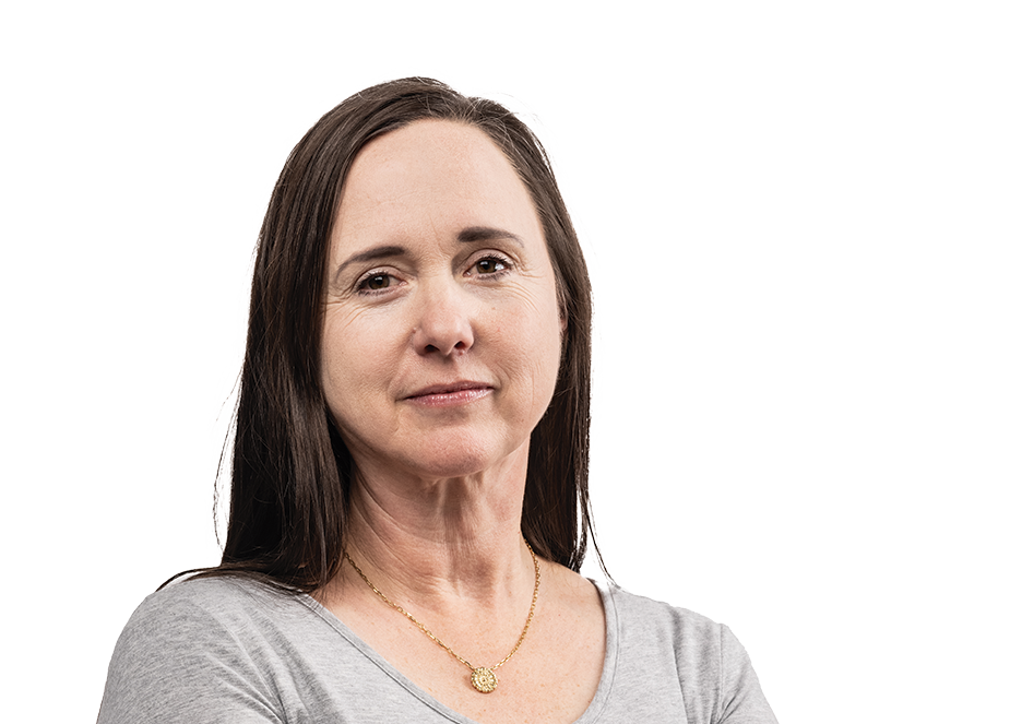 A female professor wearing a gray shirt and jeans crosses her arms.