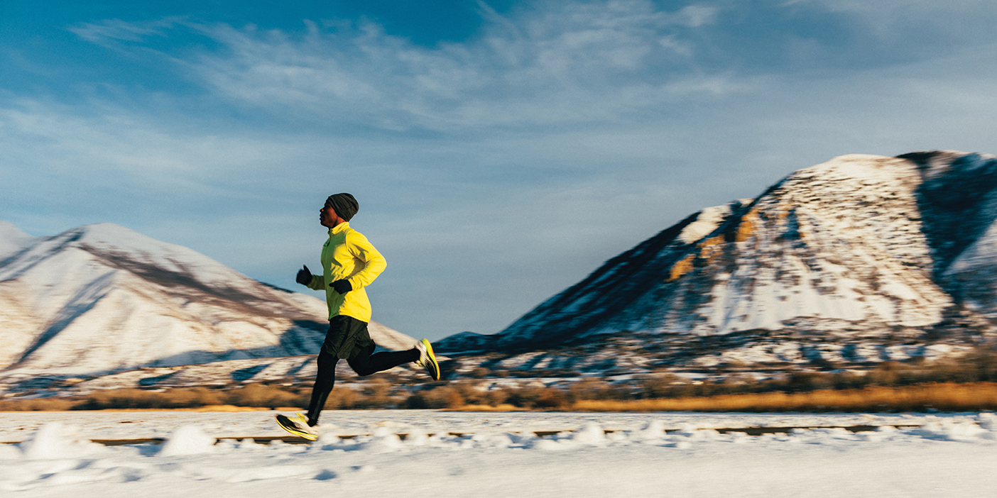 A middle aged male athlete goes for a cold, winter run in Utah, USA during a break in the snow storms. The sky is blue and the sun is shining. He is running to maintain his good mental and physical health and enjoying nature in the winter.