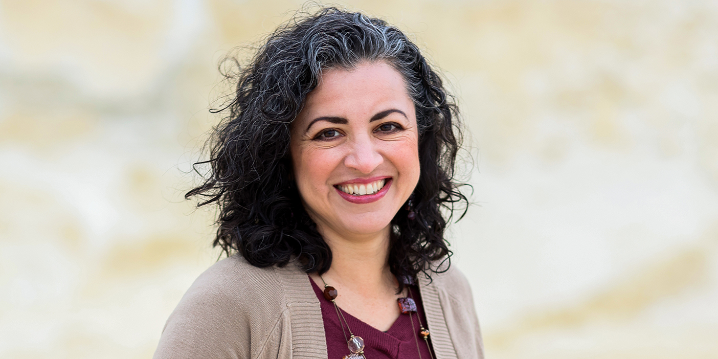 Natalia Benjamin, a woman with dark curly hair, smiles at the camera.