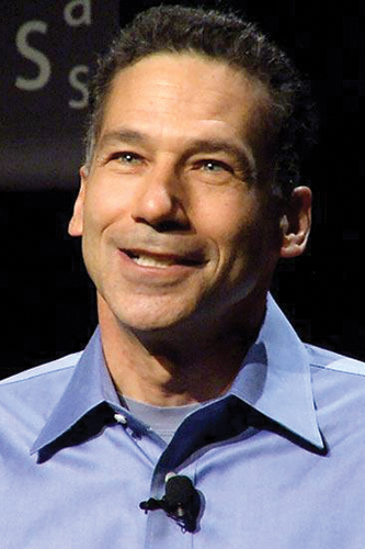 A Man in a button up blue shirt with a microphone attached to the collar speaks.