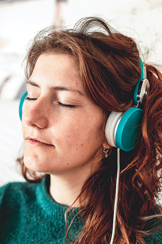 A woman closes her eyes while wearing headphones over her ears.