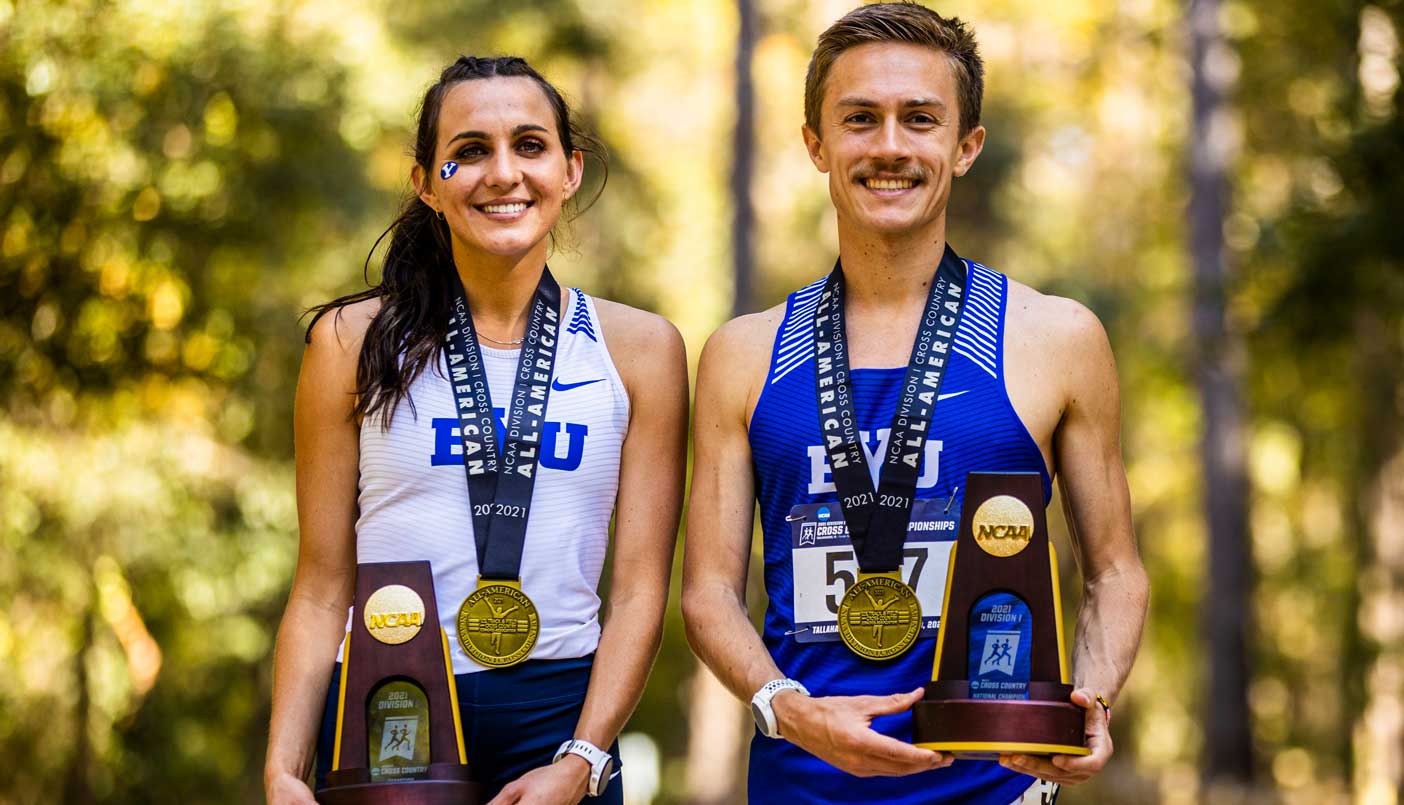 Female and male runners in BYU uniforms stand next to each other wearing first-place medals and holding trophies.