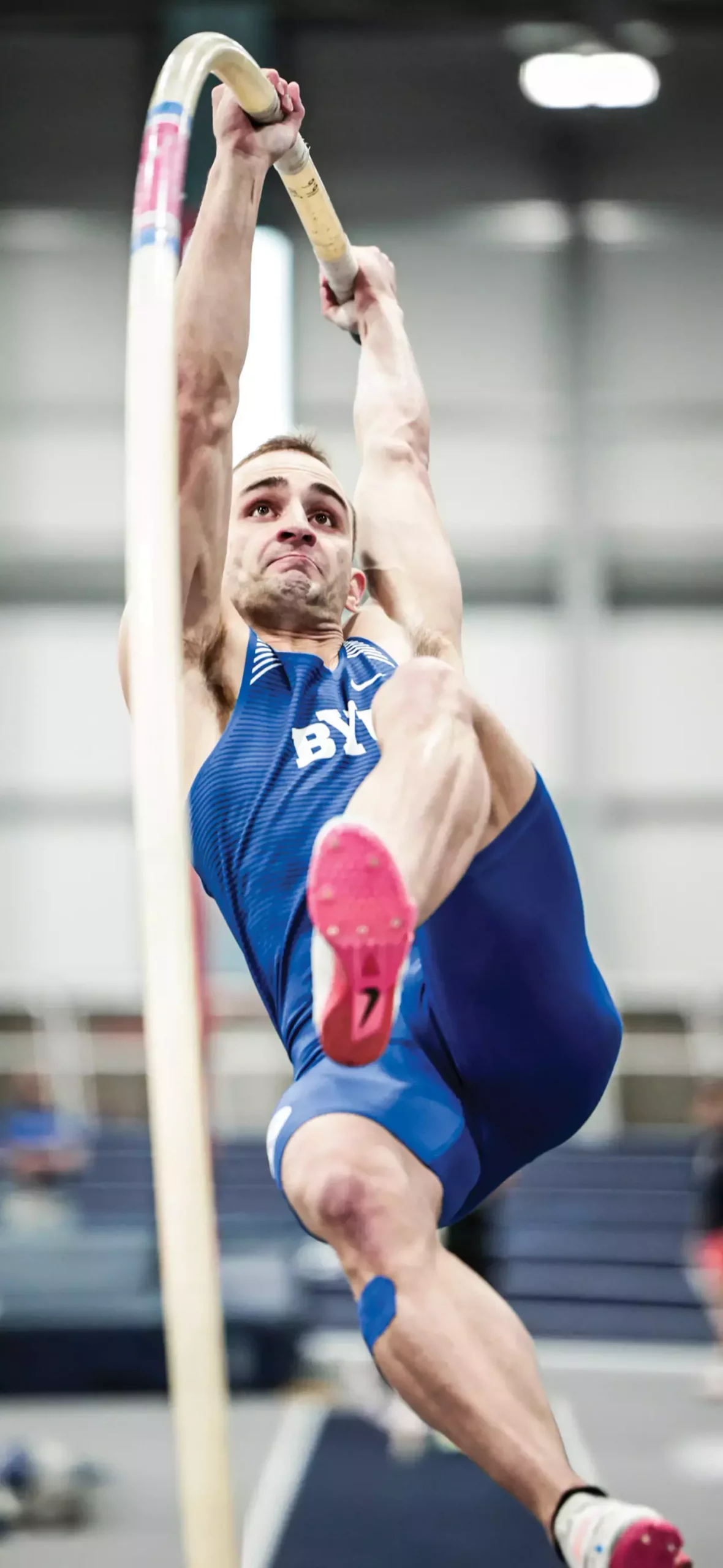 A man launches into the air holding a pole for vaulting.