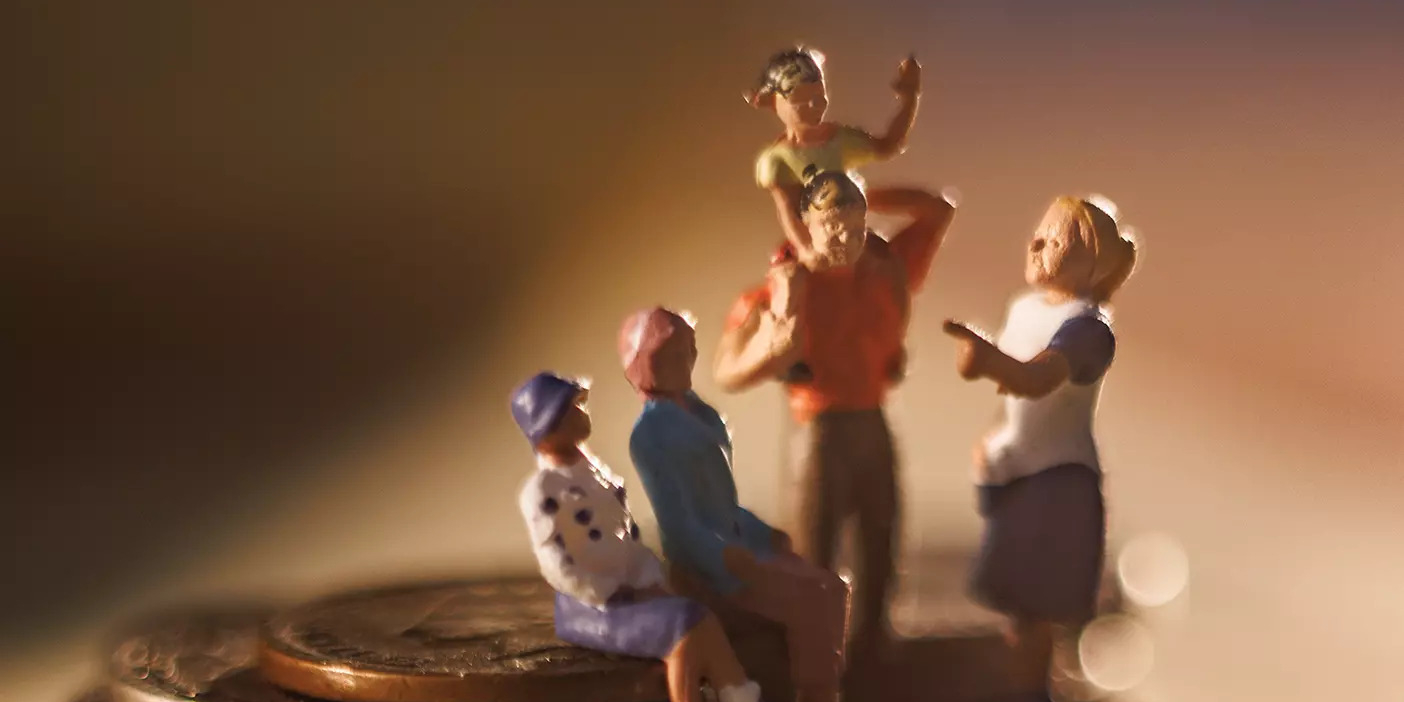 A happy figurine family stands atop a pile of coins.