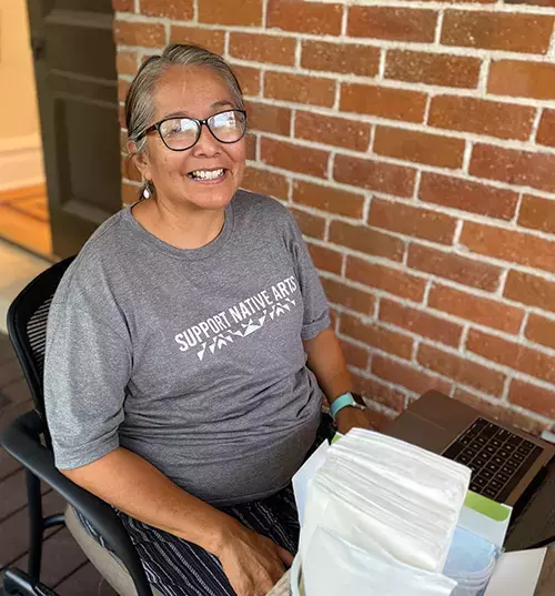 Brenda Beyal sits by her laptop, smiling brightly at the camera.