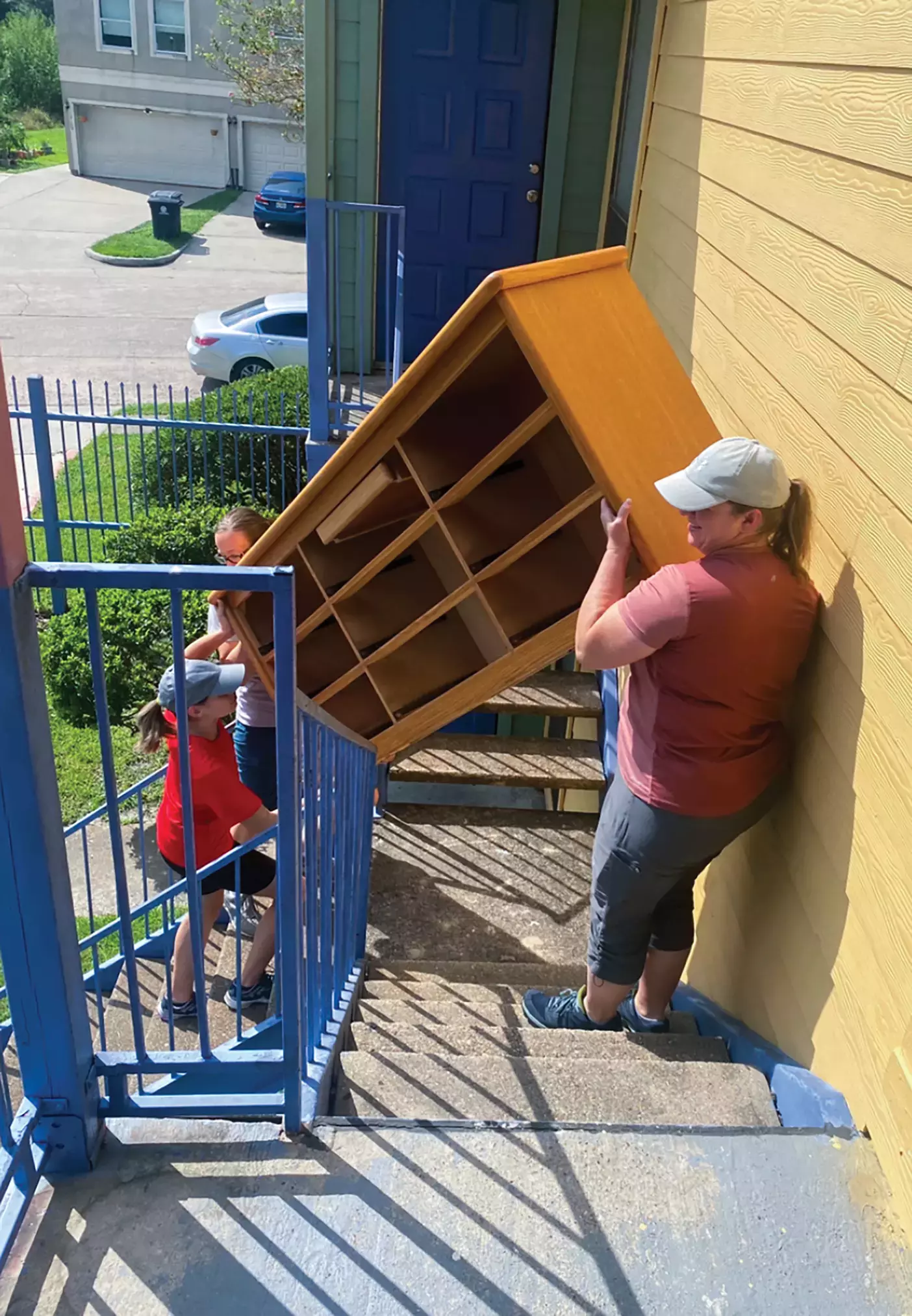 A woman and two kids help move a dresser up some apartment stairs.