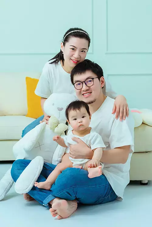 A Chinese family consisting of a woman, man, and baby. They are wearing white shirts and blue jeans.