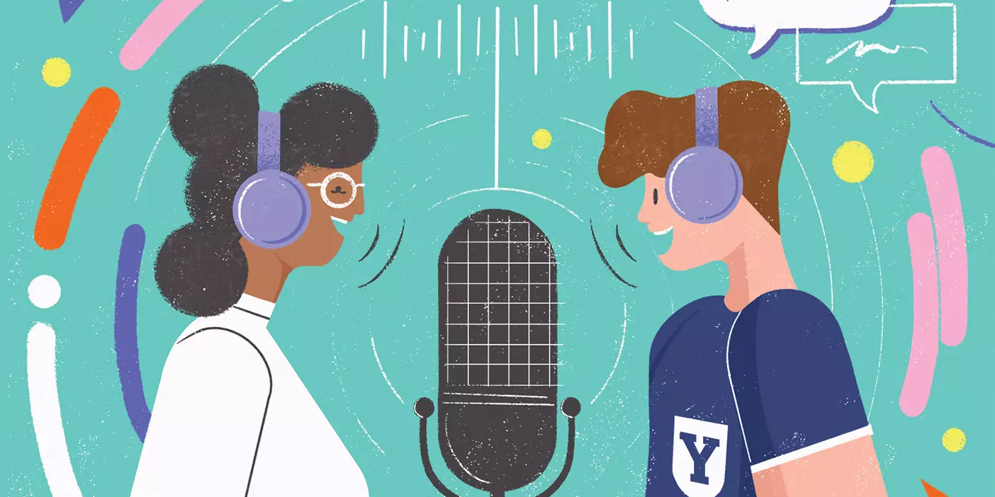 Two BYU podcasters wearing headphones stand on either side of a large microphone and speak.