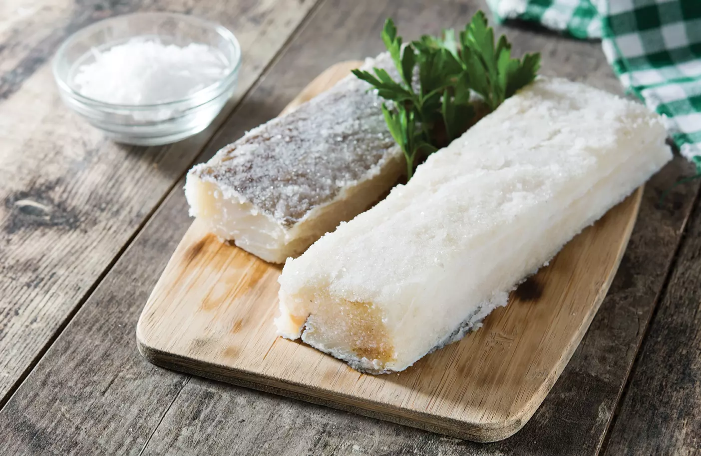 2 pieces of salted cod on a cutting board.