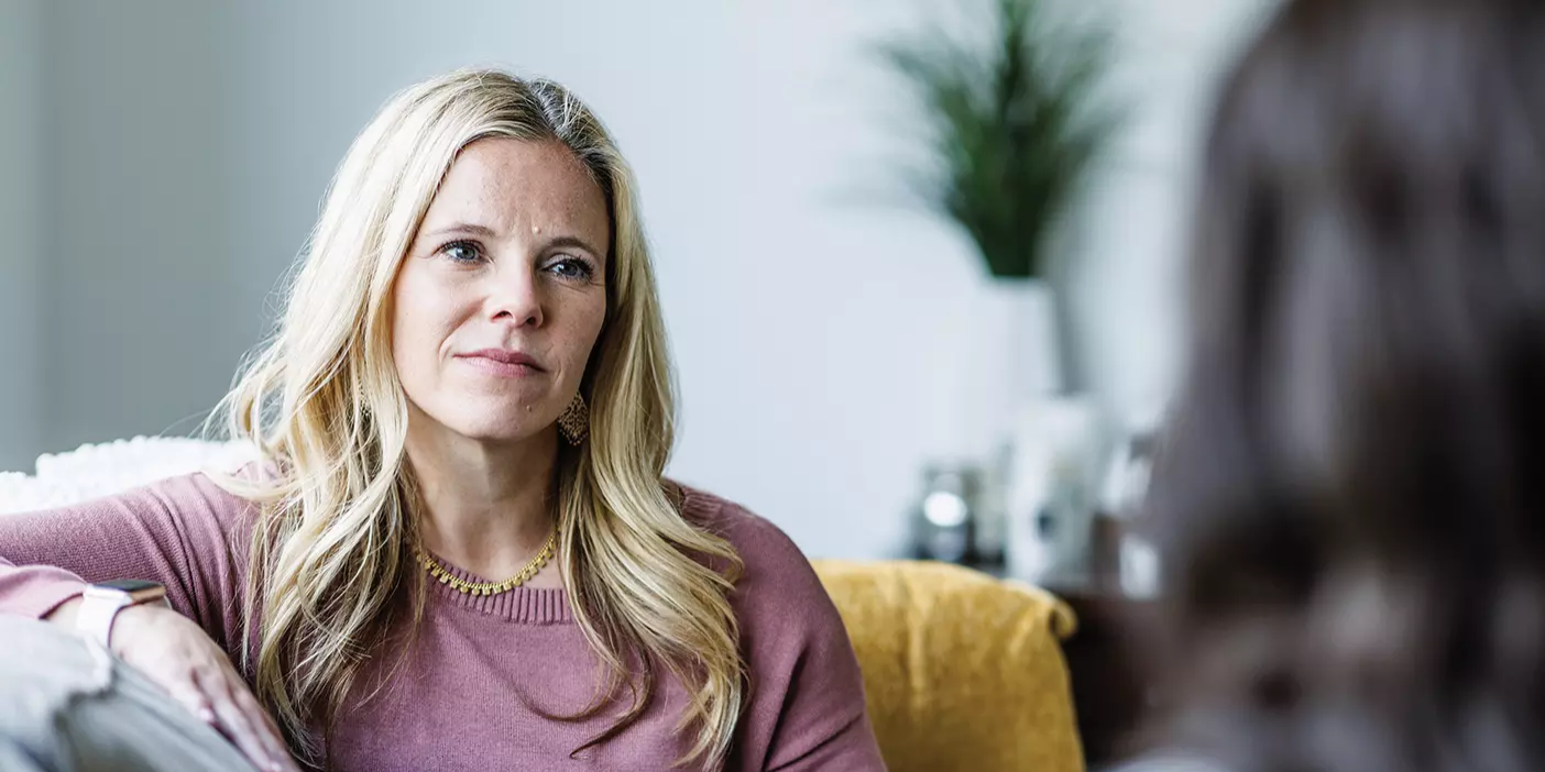 A therapist in a pink sweater sits on a couch and counsels another woman.