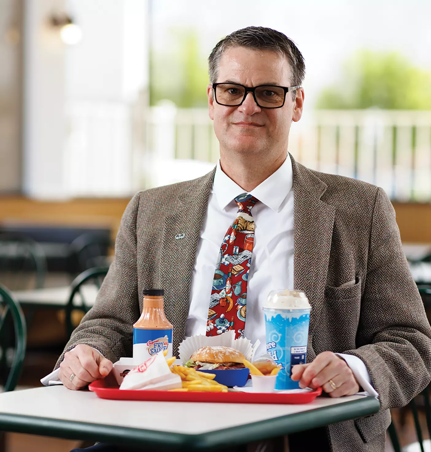 Professor Eric Eliason sits at a booth at Arctic Circle with a tray of fries, fry sauce, a pastrami burger, and a thick over-the-top milkshake.