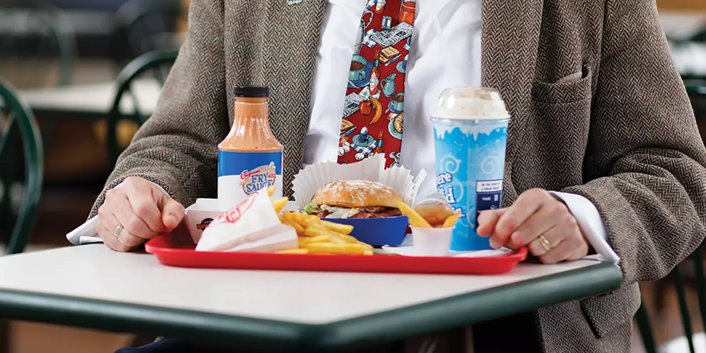 Professor Eric Eliason sits at a booth at Arctic Circle with a tray of fries, fry sauce, a pastrami burger, and a thick over-the-top milkshake.