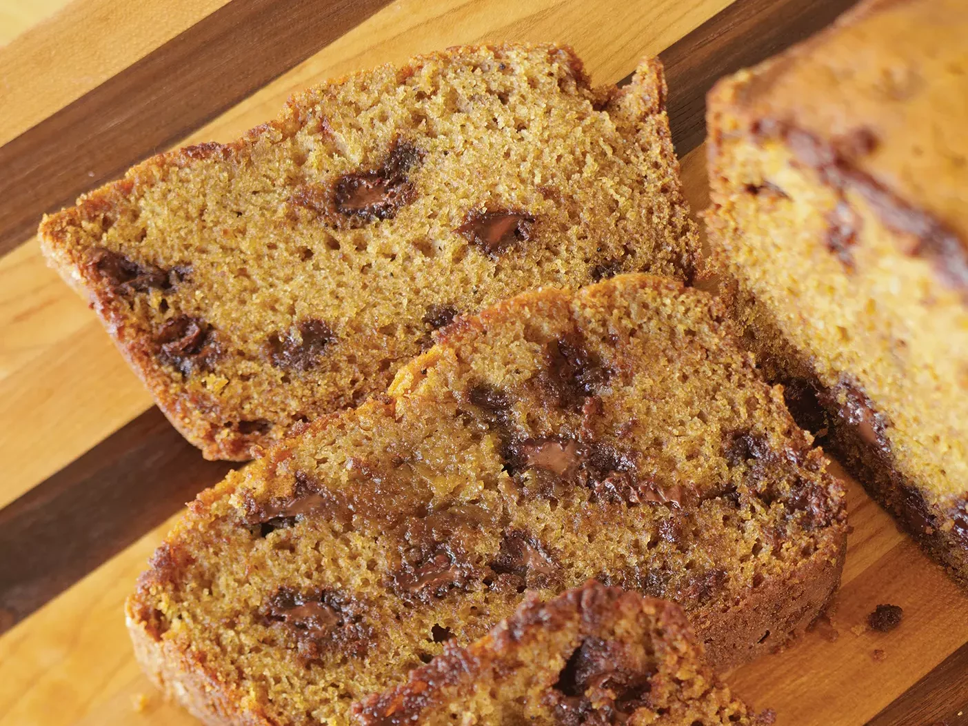 Three slices of pumpkin bread with chocolate chips on a wooden cutting board