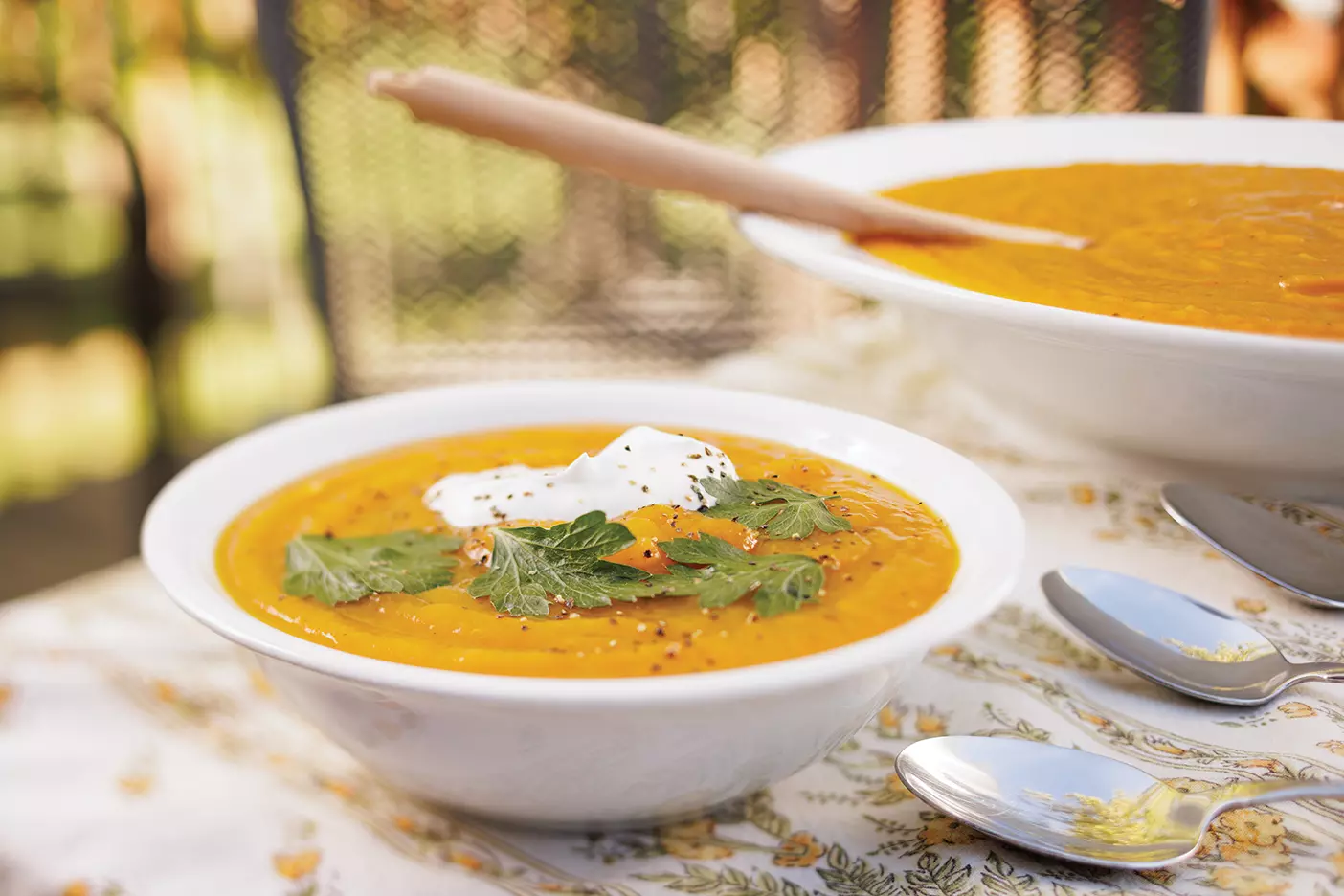 Orange pumpkin soup topped with herbs and cream is served in a white bowl.