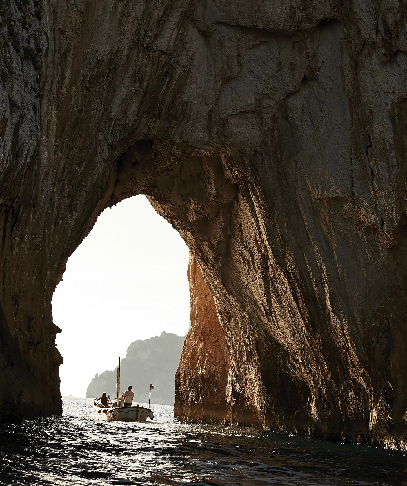 People on a boat under the arch of a coastline cave.