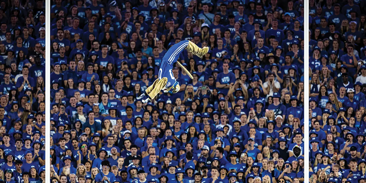 BYU's mascot Cosmo Cougar is captured up in the air, halfway through a series of three consecutive flips, centered in the field goal posts above the crowd at the BYU-Baylor football game.