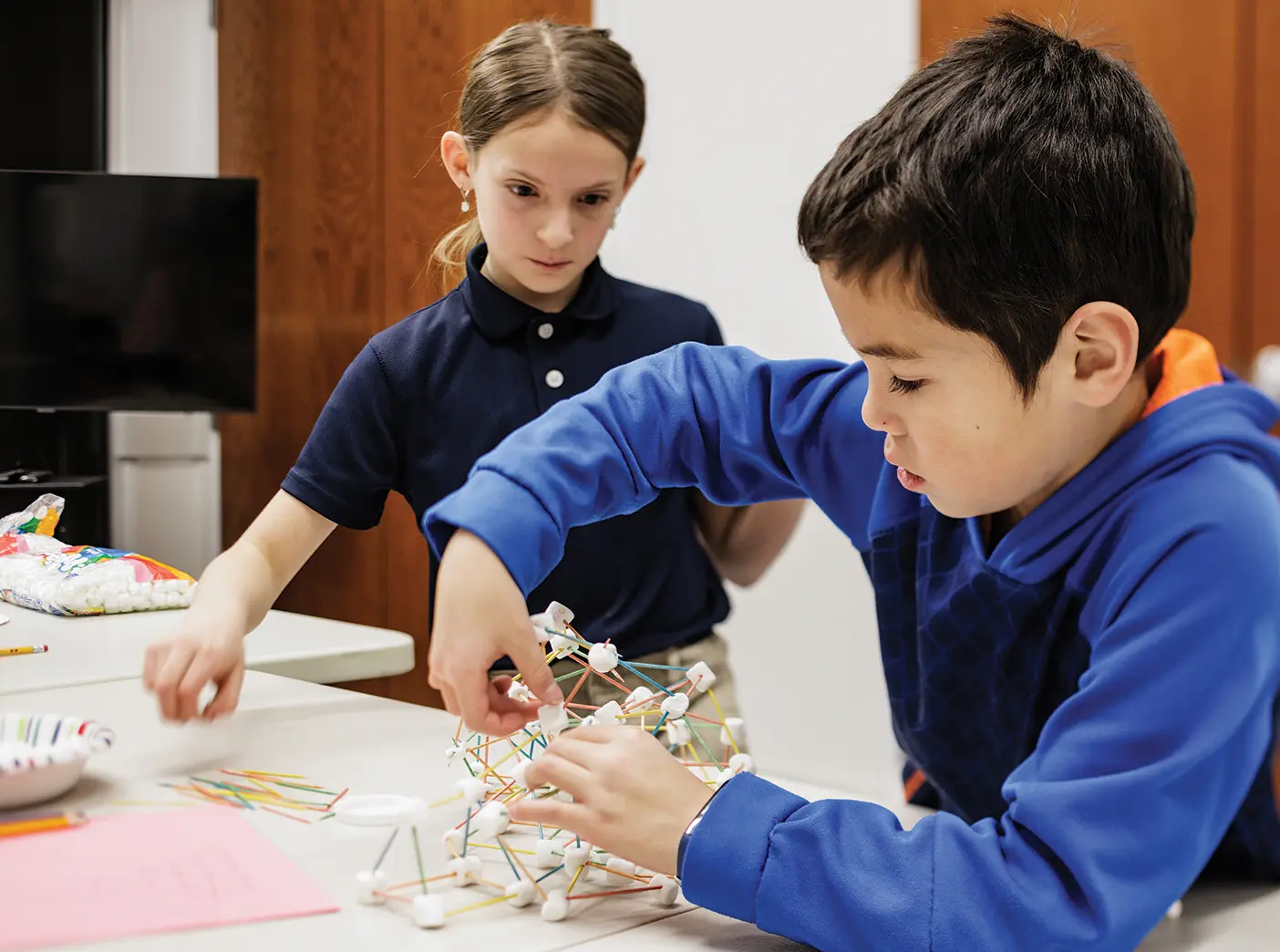 A young girl and boy build a structure out of toothpicks and mini marshmallows