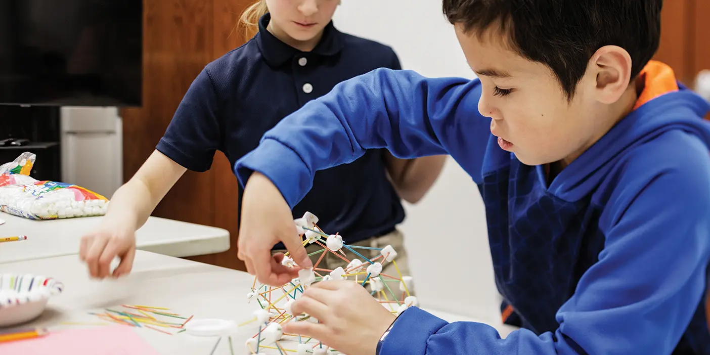 A young boy builds a structure out of toothpicks and mini marshmallows.