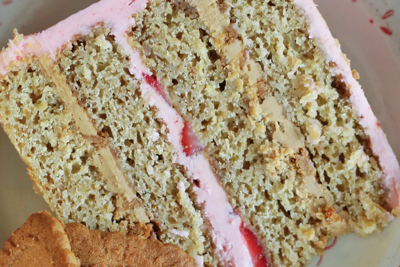 A slice of biscoff strawberry cake with pink frosting and multiple layers.